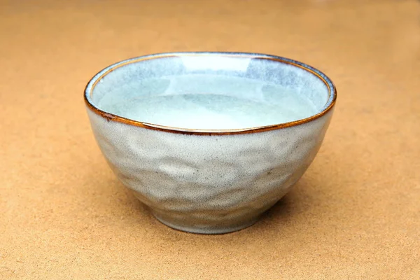 Blue ceramic  bowl with clean drink water on sand. Fresh water in bowl outdoors.