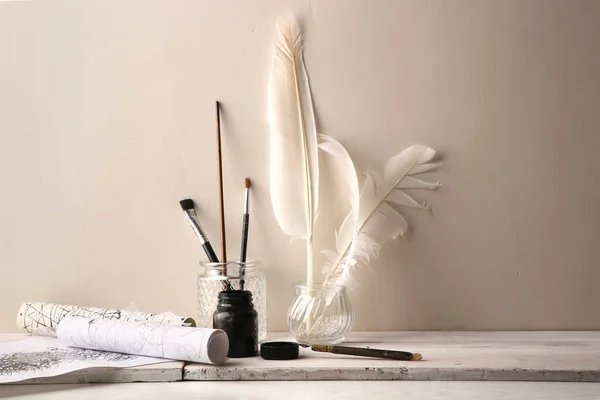 Brushes, feathers in glass ink bottles, pen, paper rollers with  ink drawing of graphic, calligraphy. Ink drawing tools of graphic or calligraphy on white wood table.