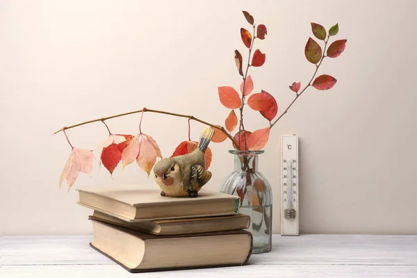 Composition of books and autumn leaves in interior. Autumn still life with decorative bird sparrow, books, bouquet and thermometer.