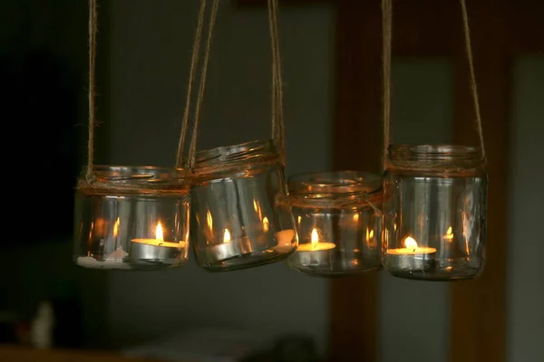 Aromatic candles in jars hanging in interior. DIY candles in glass jars hanging on linen jute.