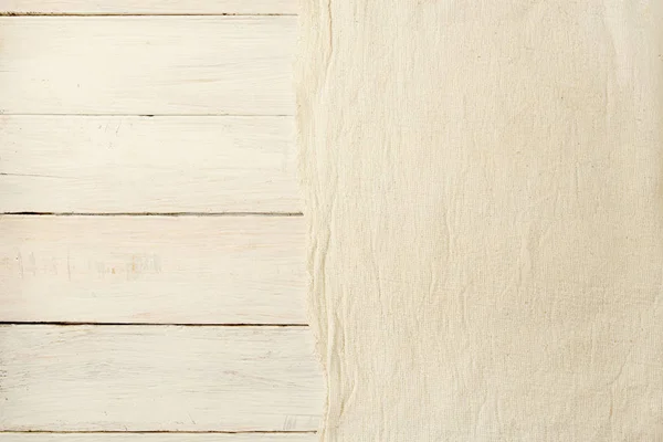 Beige woven cloth on wooden  background. Fabric canvas on white planking with empty place.