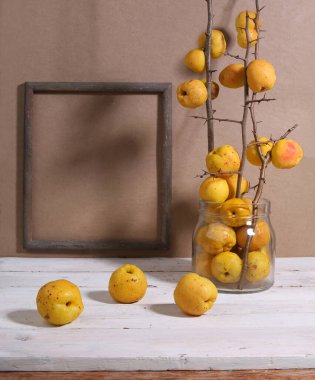 Cam kavanozda Chaenomeles meyveleri ve fotokopi alanı olan çerçeve. Beyaz ahşap masa üzerinde olgun meyvelerle Maules ayva çalısı hala hayat. Yenilebilir turunçgiller.