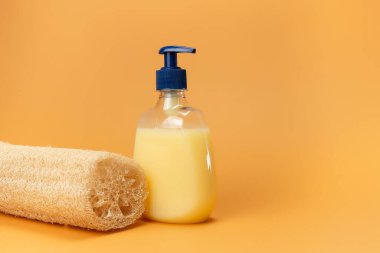 Bir şişe sarı sıvı sabun ve doğal malzemeden yapılmış bir bej arkaplandaki bitkinin kökü. Temiz eller kavramı. Şampuan, Sıvı Sabun, Aromatik Banyo Tuzu ve Diğer Tuvaletler.