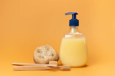 Bir şişe sıvı sabun sarısı ve bej arka planda doğal malzemeden yapılmış süngerli bambu diş fırçası. Temiz eller kavramı. Şampuan, Sıvı Sabun, Aromatik Banyo Tuzu ve Diğer Tuvaletler.