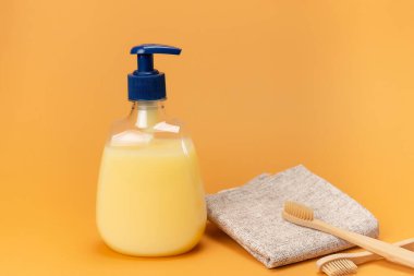 Bir şişe sıvı sabun sarısı ve bej arka planda doğal malzemeden yapılmış süngerli bambu diş fırçası. Temiz eller kavramı. Şampuan, Sıvı Sabun, Aromatik Banyo Tuzu ve Diğer Tuvaletler.