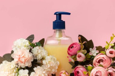 Sarı sıvı sabun şişesi ve pembe arka planda güzel narin çiçekler. Temiz eller kavramı. Şampuan, Sıvı Sabun, Aromatik Banyo Tuzu ve Diğer Tuvaletler.