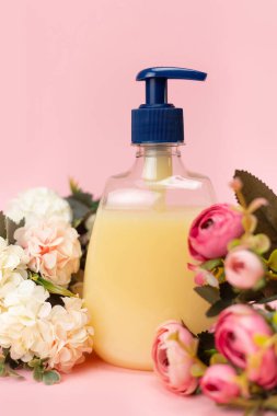 Sarı sıvı sabun şişesi ve pembe arka planda güzel narin çiçekler. Temiz eller kavramı. Şampuan, Sıvı Sabun, Aromatik Banyo Tuzu ve Diğer Tuvaletler.