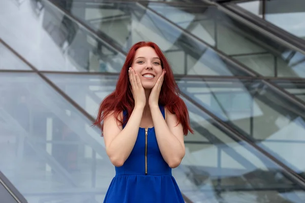 Pretty young woman with a wonderful sense of humor, red hair and a blue dress on a city street laughing at the camera