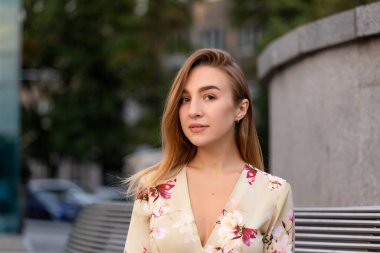 Mavi bir iş merkezinin arka planında bej bir elbise giymiş güzel bir genç kızın portresi.