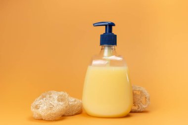 Bir şişe sarı sıvı sabun ve doğal malzemeden yapılmış bir bej arkaplandaki bitkinin kökü. Temiz eller kavramı. Şampuan, Sıvı Sabun, Aromatik Banyo Tuzu ve Diğer Tuvaletler.