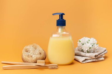 Bir şişe sıvı sabun sarısı ve bej arka planda doğal malzemeden yapılmış süngerli bambu diş fırçası. Temiz eller kavramı. Şampuan, Sıvı Sabun, Aromatik Banyo Tuzu ve Diğer Tuvaletler.
