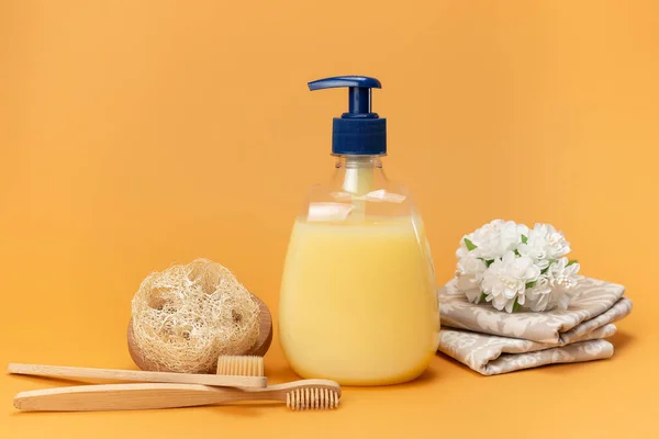 Bottle of liquid soap yellow and bamboo toothbrushes with a sponge made of natural material on a beige background. Clean hands concept. Shampoo, Liquid Soap, Aromatic Bath Salt And Other Toiletry.