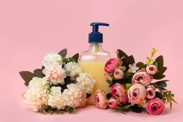 Sarı sıvı sabun şişesi ve pembe arka planda güzel narin çiçekler. Temiz eller kavramı. Şampuan, Sıvı Sabun, Aromatik Banyo Tuzu ve Diğer Tuvaletler.