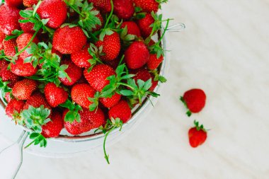 Kırsal beyaz ahşap arka planda kasede taze çilek yığını.