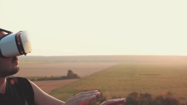 Jovem usa óculos de realidade virtual na natureza em um belo pôr do sol — Vídeo de Stock