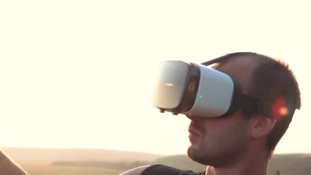 Jovem usa óculos de realidade virtual na natureza em um belo pôr do sol — Vídeo de Stock