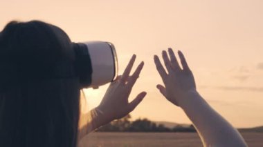 Altın buğday tarlasında güzel bir kız gün batımında sanal gerçeklik gözlüğü kullanıyor.