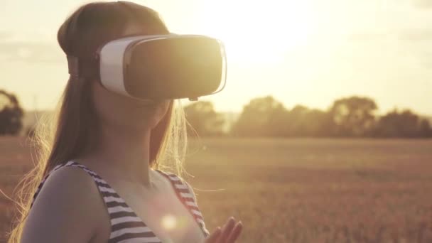 Hermosa chica en un campo de trigo dorado utiliza gafas de realidad virtual en la puesta de sol en cámara lenta — Vídeo de stock