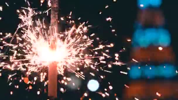 Bengalfeuer brennt in Zeitlupe vor dem Hintergrund eines blinkenden Weihnachtsbaums — Stockvideo