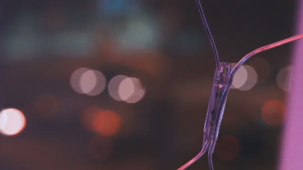 Christmas garland with colorful lights by the window against the background of the city and the movement of cars, close-up. Blurred Christmas lights. Bokeh. — Stock Video