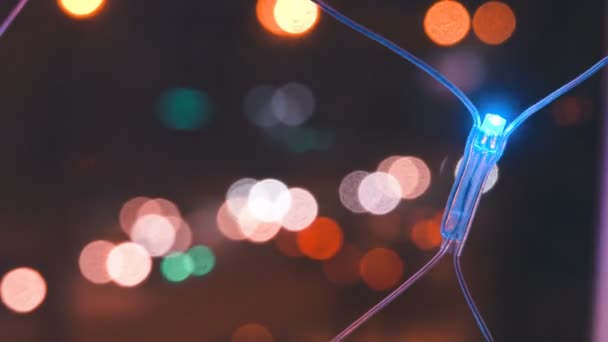 Christmas garland with colorful lights by the window against the background of the city and the movement of cars, close-up. Blurred Christmas lights. Bokeh. — Stock Video