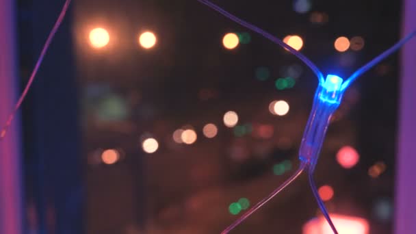 Christmas garland med färgglada lampor av fönstret mot bakgrund av staden och förflyttning av bilar, närbild. Suddig julbelysning. Bokeh. — Stockvideo
