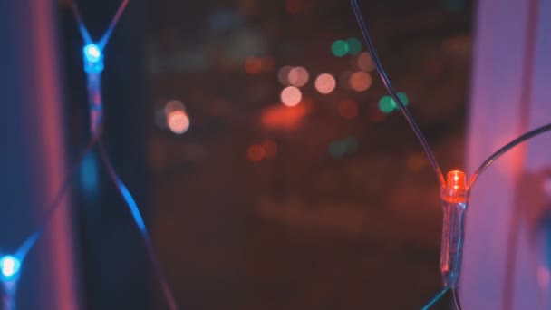 Ghirlanda di Natale con luci colorate dalla finestra sullo sfondo della città e il movimento delle auto, primo piano. Luci di Natale offuscate. Bokeh . — Video Stock