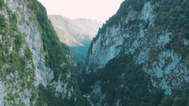 Dağların havadan 4k görünümü. Gün batımında ağaçlar ve bitki örtüsü ile büyümüş güçlü kayalıklar arasında dağların geçitçarpıcı bir geçit