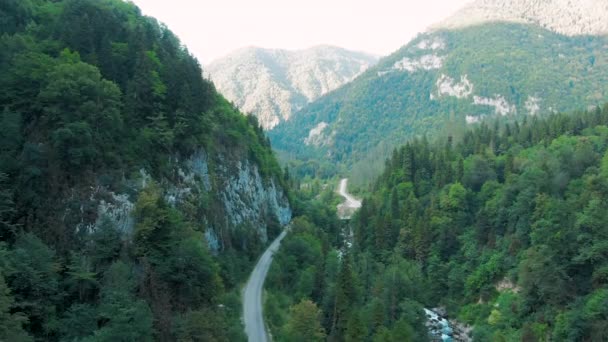 Vista aérea 4K das montanhas. Uma passagem deslumbrante no desfiladeiro das montanhas entre os poderosos penhascos cobertos de árvores e vegetação ao pôr do sol — Vídeo de Stock