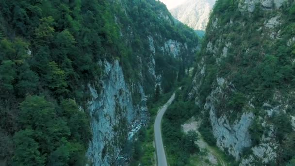 Vista aérea 4K das montanhas. Uma passagem deslumbrante no desfiladeiro das montanhas entre os poderosos penhascos cobertos de árvores e vegetação ao pôr do sol — Vídeo de Stock