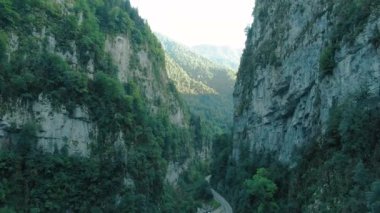 Dağların havadan 4k görünümü. Gün batımında ağaçlar ve bitki örtüsü ile büyümüş güçlü kayalıklar arasında dağların geçitçarpıcı bir geçit