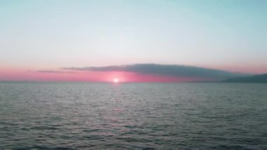 Havadan 4k görünüm. Deniz üzerinde çarpıcı gün batımı güneşi. Güzel sinema sahnesi. Altın güneş ufukta batıyor, su yüzeyinin üzerinde uçuyor.