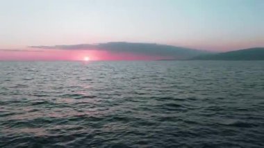 Havadan 4k görünüm. Deniz üzerinde çarpıcı gün batımı güneşi. Güzel sinema sahnesi. Altın güneş ufukta batıyor, su yüzeyinin üzerinde uçuyor.