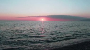 Havadan 4k görünüm. Deniz üzerinde çarpıcı gün batımı güneşi. Güzel sinema sahnesi. Altın güneş ufukta batıyor, su yüzeyinin üzerinde uçuyor.