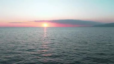 Havadan 4k görünüm. Deniz üzerinde çarpıcı gün batımı güneşi. Güzel sinema sahnesi. Altın güneş ufukta batıyor, su yüzeyinin üzerinde uçuyor.