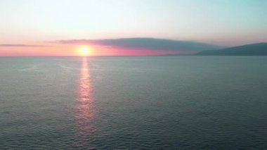 Havadan 4k görünüm. Deniz üzerinde çarpıcı gün batımı güneşi. Güzel sinema sahnesi. Altın güneş ufukta batıyor, yavaş çekimde su yüzeyinin üzerinde uçuyor