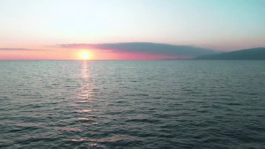 Havadan 4k görünüm. Deniz üzerinde çarpıcı gün batımı güneşi. Güzel sinema sahnesi. Altın güneş ufukta batıyor, yavaş çekimde su yüzeyinin üzerinde uçuyor