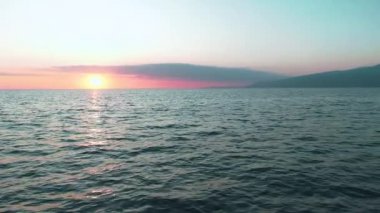 Havadan 4k görünüm. Deniz üzerinde çarpıcı gün batımı güneşi. Güzel sinema sahnesi. Altın güneş ufukta batıyor, yavaş çekimde su yüzeyinin üzerinde uçuyor