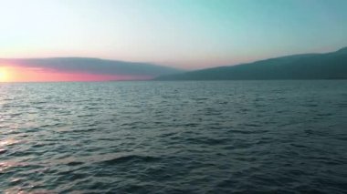 Havadan 4k görünüm. Deniz üzerinde çarpıcı gün batımı güneşi. Güzel sinema sahnesi. Altın güneş ufukta batıyor, yavaş çekimde su yüzeyinin üzerinde uçuyor