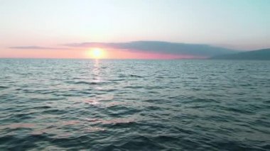 Havadan 4k görünüm. Deniz üzerinde çarpıcı gün batımı güneşi. Güzel sinema sahnesi. Altın güneş ufukta batıyor, yavaş çekimde su yüzeyinin üzerinde uçuyor