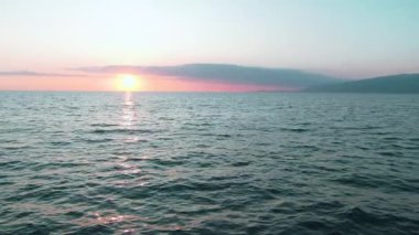 Havadan 4k görünüm. Deniz üzerinde çarpıcı gün batımı güneşi. Güzel sinema sahnesi. Altın güneş ufukta batıyor, yavaş çekimde su yüzeyinin üzerinde uçuyor