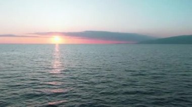 Havadan 4k görünüm. Deniz üzerinde çarpıcı gün batımı güneşi. Güzel sinema sahnesi. Altın güneş ufukta batıyor, su yüzeyinin üzerinde uçuyor.