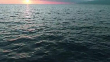 Havadan 4k görünüm. Deniz üzerinde çarpıcı gün batımı güneşi. Güzel sinema sahnesi. Altın güneş ufukta batıyor, su yüzeyinin üzerinde uçuyor.