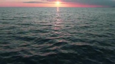 Havadan 4k görünüm. Deniz üzerinde çarpıcı gün batımı güneşi. Güzel sinema sahnesi. Altın güneş ufukta batıyor, su yüzeyinin üzerinde uçuyor.