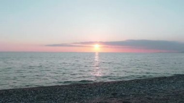 Havadan 4k görünüm. Deniz üzerinde çarpıcı gün batımı güneşi. Güzel sinema sahnesi. Altın güneş ufukta batıyor, su yüzeyinin üzerinde uçuyor.