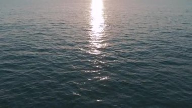 Havadan 4k görünüm. Deniz üzerinde çarpıcı gün batımı güneşi. Güzel sinema sahnesi. Altın güneş ufukta batıyor, yavaş çekimde su yüzeyinin üzerinde uçuyor
