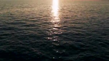 Havadan 4k görünüm. Deniz üzerinde çarpıcı gün batımı güneşi. Güzel sinema sahnesi. Altın güneş ufukta batıyor, su yüzeyinin üzerinde uçuyor.