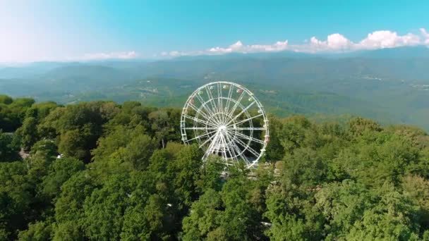 Vista aérea 4k. Uma roda gigante gira no topo de uma montanha. Vistas deslumbrantes das montanhas e do mar. Atração para adultos e crianças — Vídeo de Stock