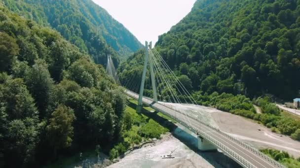 Havadan 4k görünüm. Nehir üzerinde asma köprü. Dağlar ve kayalar arasında köprü üzerinde uçan. — Stok video