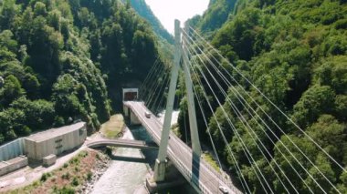 Havadan 4k görünüm. Nehir üzerinde asma köprü. Dağlar ve kayalar arasında köprü üzerinde uçan.